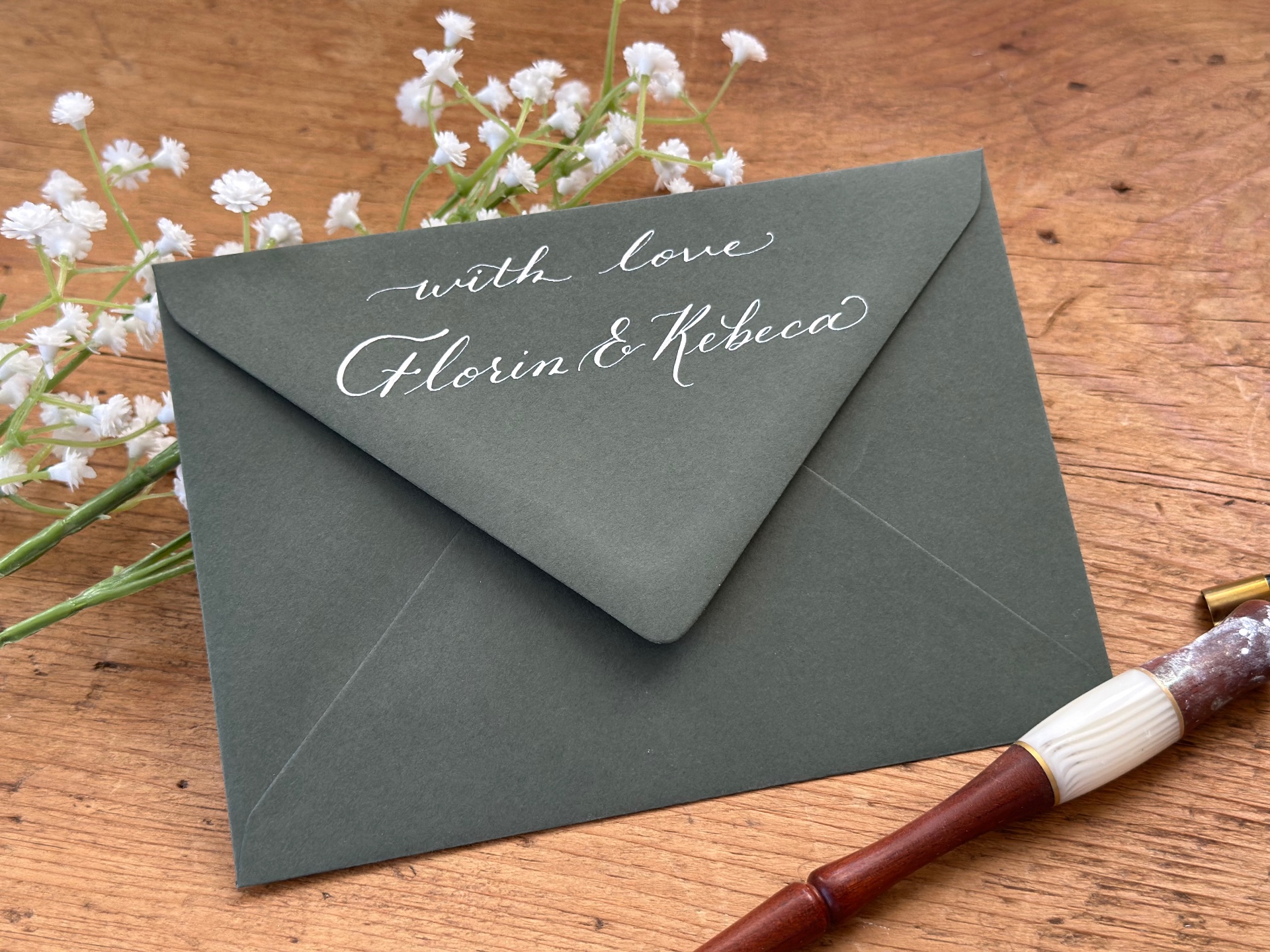 Handwritten white calligraphy on a dark green wedding envelope