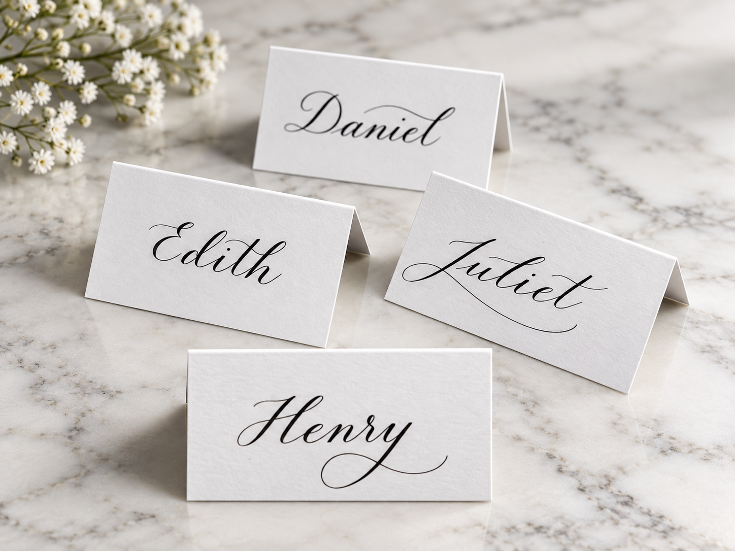 Folded white place cards with handwritten names on marble