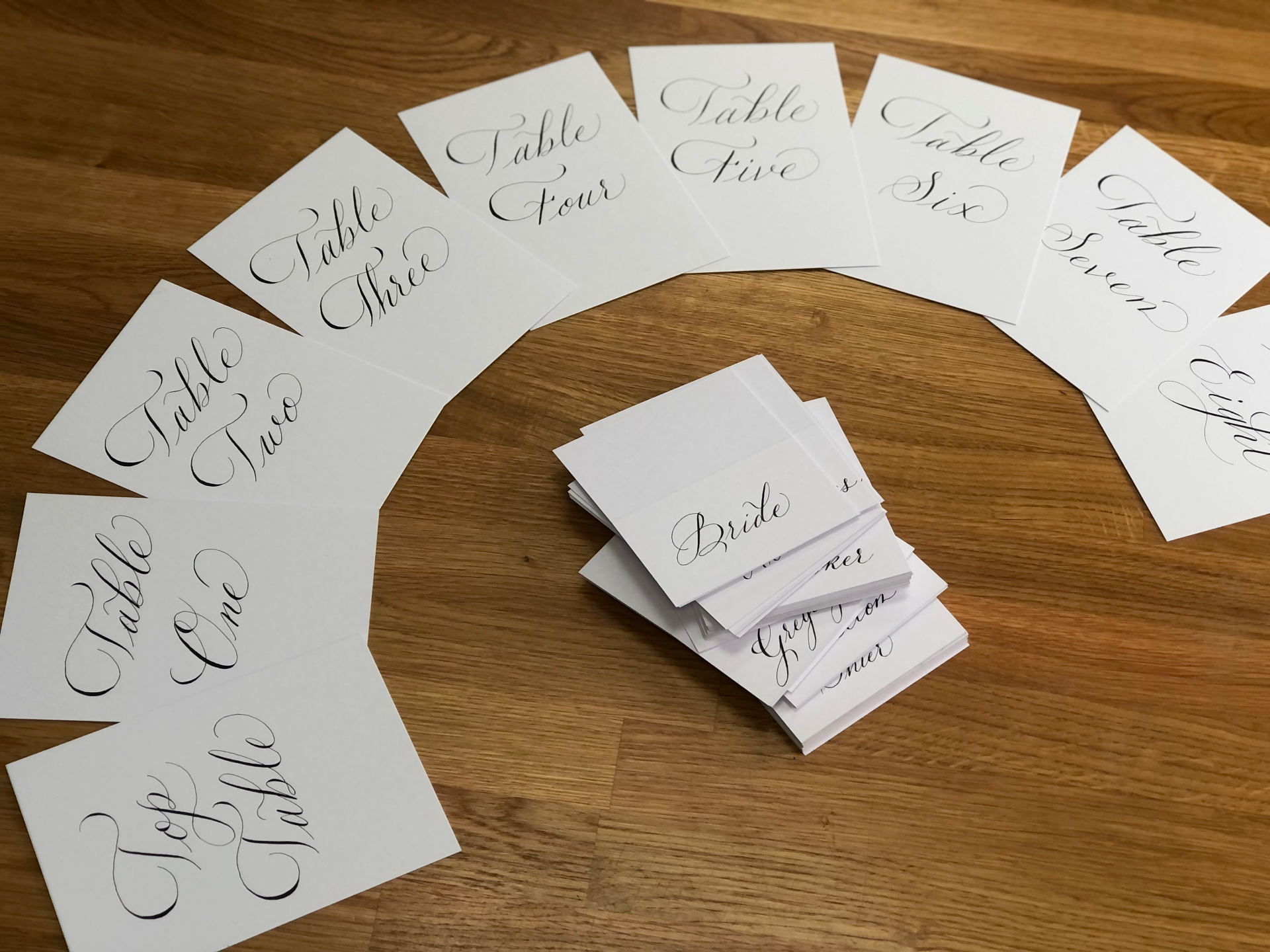 Handwritten table number cards and folded place cards laid out on wood